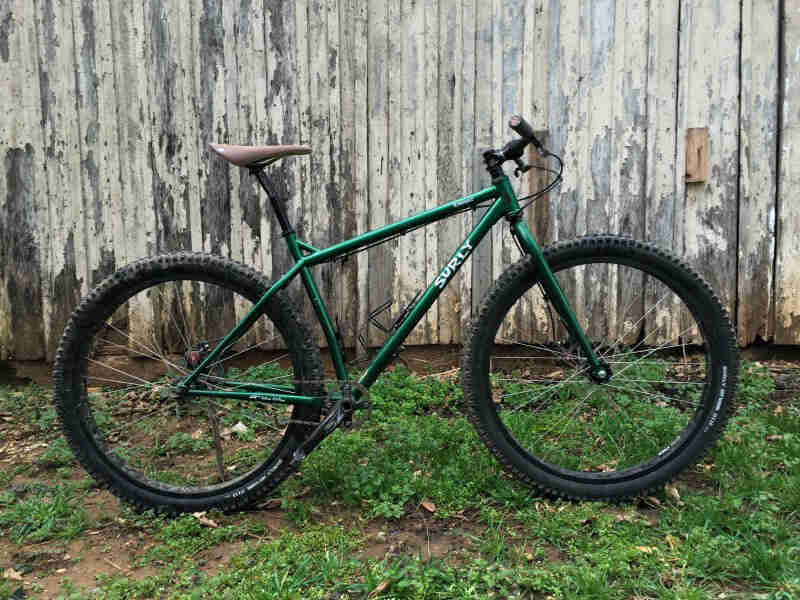 Surly Krampus bike - green - right side view - parked on grass in front of a wood wall with chipped paint