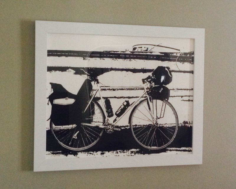 A black and white framed picture on a wall, showing a right side view of a Surly bike with gear
