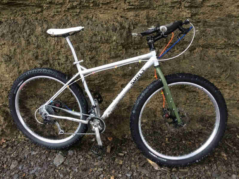Right side view of a white Surly bike, with olive drab forks, parked along the bottom of a cliff wall