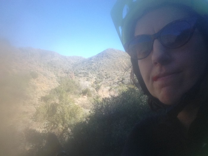 Hazy head shot of a person wearing a helmet and sunglasses, with desert hills behind, in the background