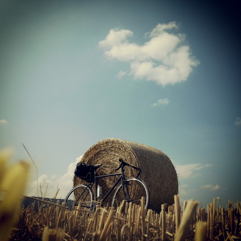 Right side view of a black Surly bike, with a rear pack, leaning against a rolled bale of hay