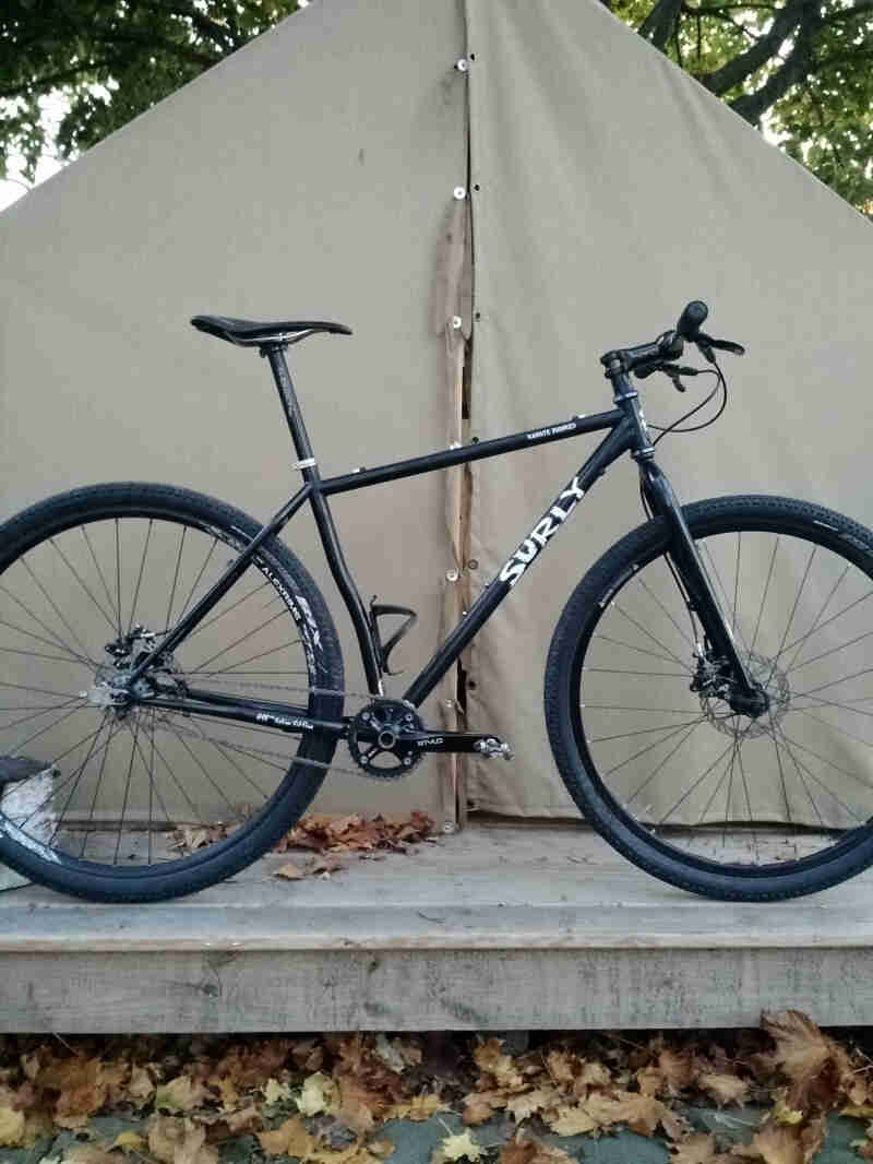 Right profile of a Surly Karate Monkey bike, black, parked in front of a green tent