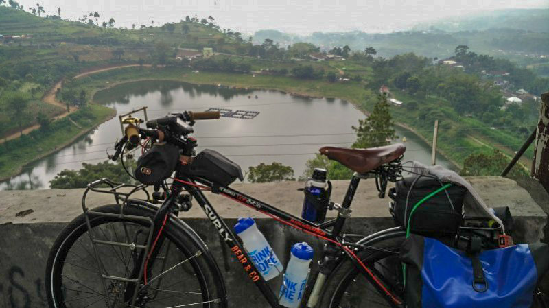 Left side view of a black Surly bike, loaded with gear, in front of a cement wall, overlooking a pond down below