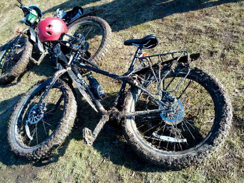 Downward view of 2 muddy Surly fat bikes, laying on their right side on grass