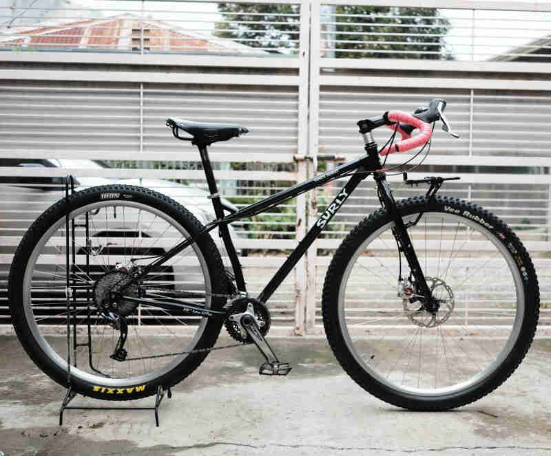 Right side view of a black Surly bike, parked on a sidewalk, in front of a white fence