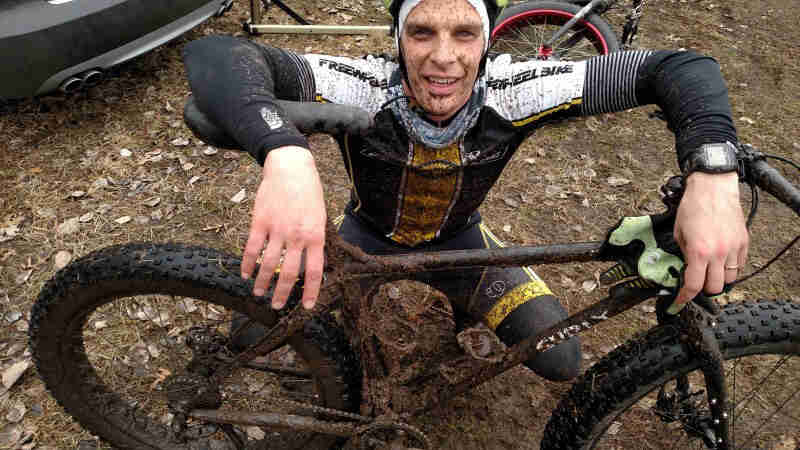 Downward, right side view of a muddy, black Surly fat bike, with a dirty cyclist, squatting down behind