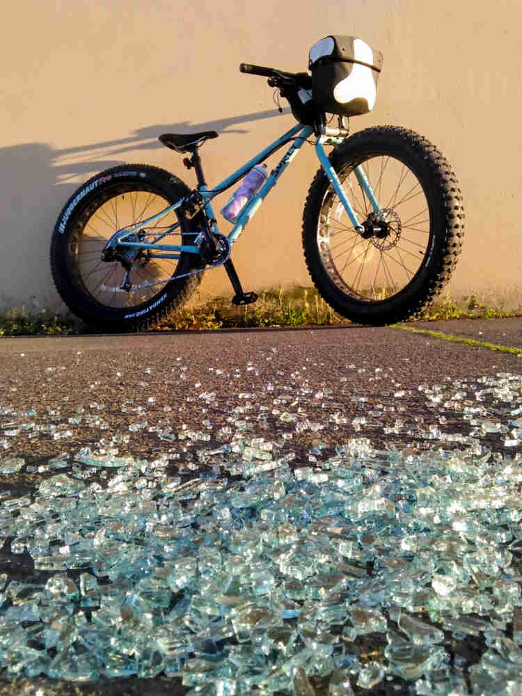 Right side view of a Surly fat bike, parked at the end of a parking spot with broken glass, next to a tan wall