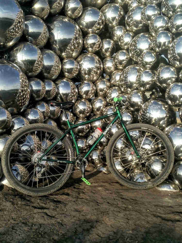 Right profile of a Surly Krampus bike, green, standing in dirt, in front of a wall of chrome spheres
