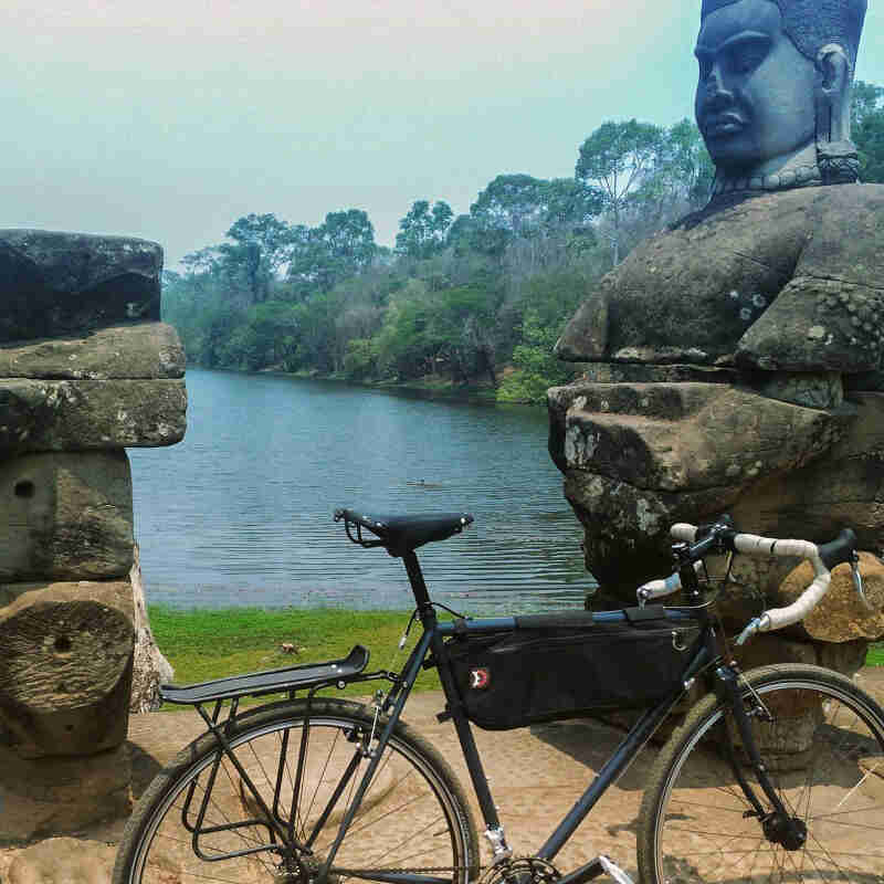 Right side view of a Surly bike, parked on dirt in front of a Buddha statue, with a pond and trees in the background