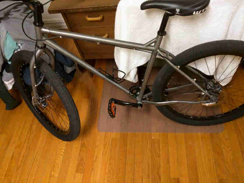 Downward left side view of a gray Surly bike, parked in a room on a wood floor