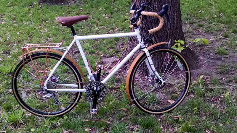 Right side view of a white Surly bike, standing in grass, in front of the base of a tree