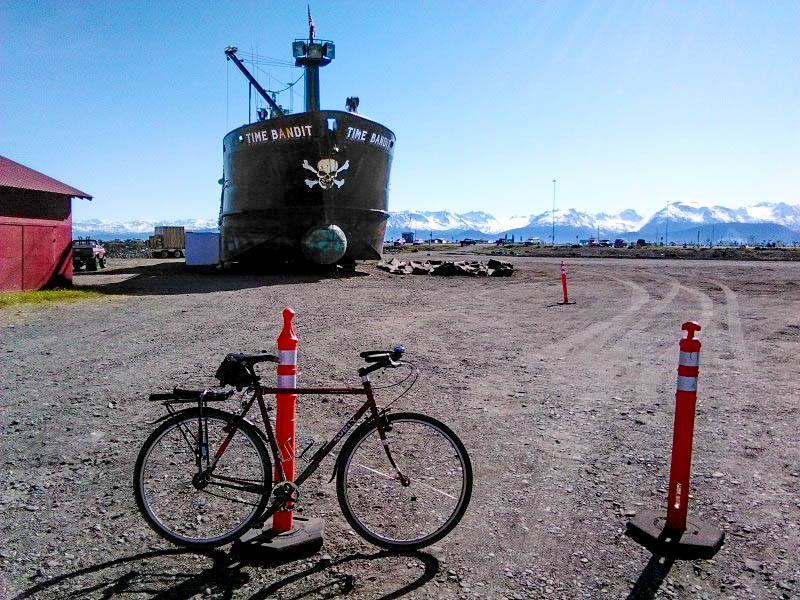 Right side view of Surly bike, leaning on a traffic cone, on a gravel lot with a land bound ship and mountains behind