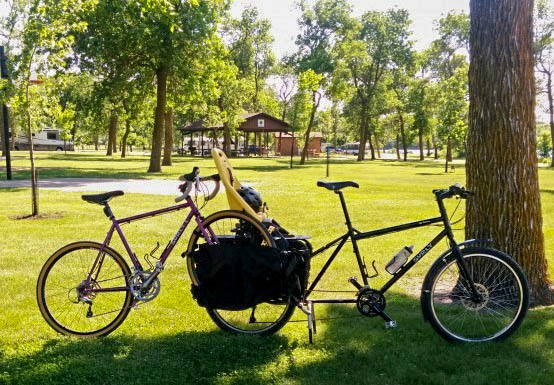 Right side view of a bike with saddle bags, with another bike propped on back, in a grass field at a park