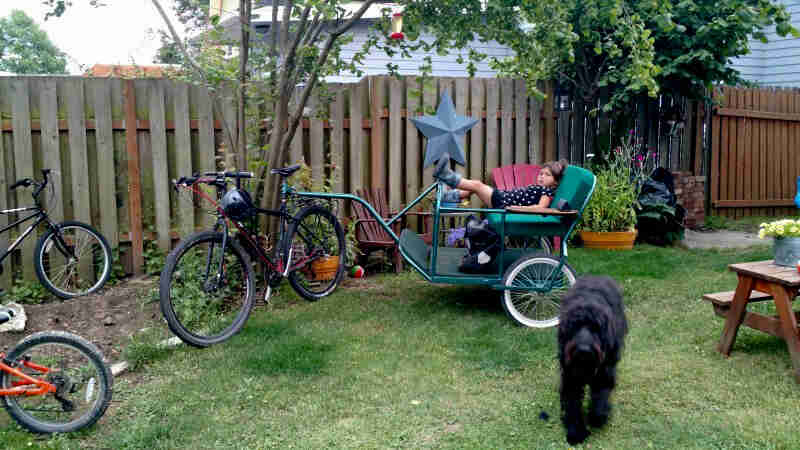 A Surly bike with a child side on the trailer behind in backyard with a black dog
