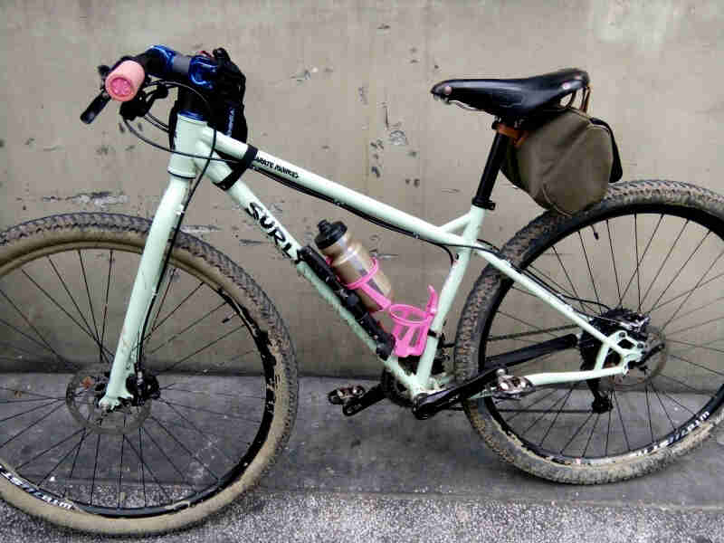 Left side view of a Surly Karate Monkey, mint, parked on a cement, next to a concrete wall