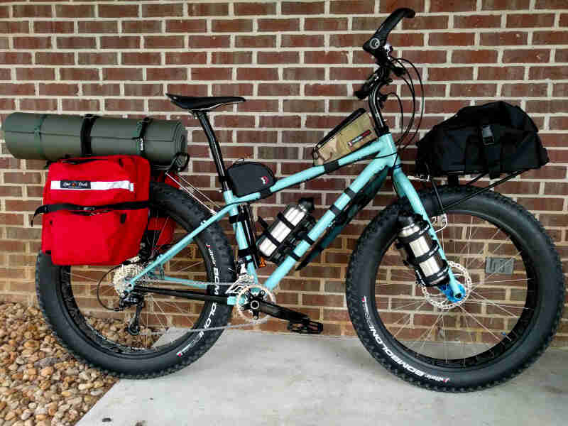 Right side view of a Surly fat bike, loaded with gear, parked on concrete in front of a red brick wall