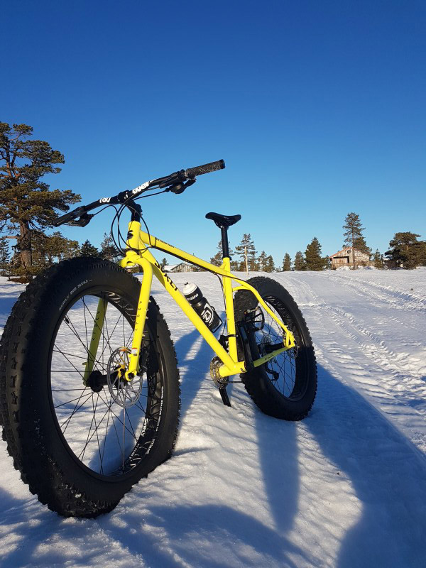 Front left view of a Surly fat bike, yellow, facing down a snow covered hill