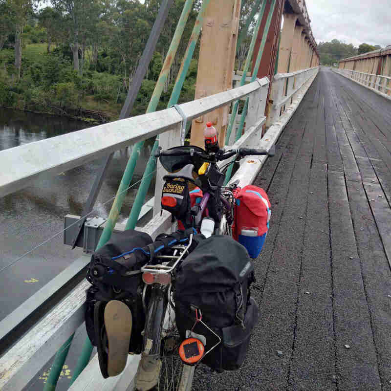 Rear view of a Surly bike leaning on rail, facing down a bridge over a river