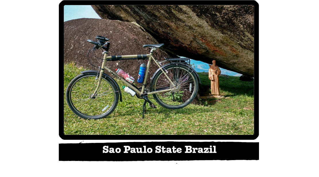 Left side view of a Surly bike on grass, in front of 2 giant boulders - Sao Paulo State Brazil tag below image