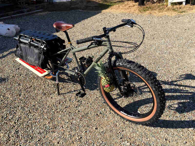 Downward, right side view of an olive Big Fat Dummy bike, parked in a gravel lot