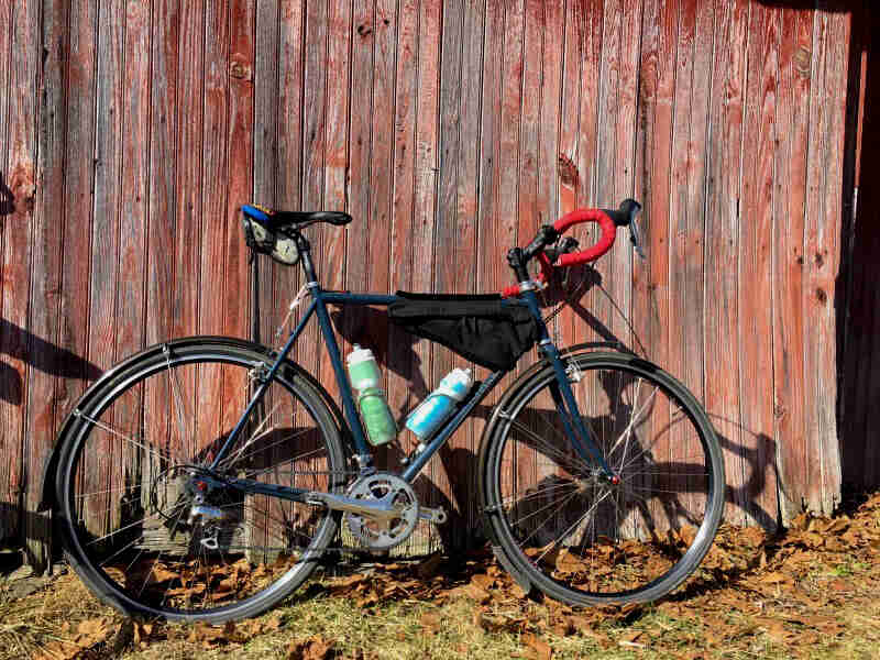 Right side view of a green Cross Check bike, parked along a red barn wall