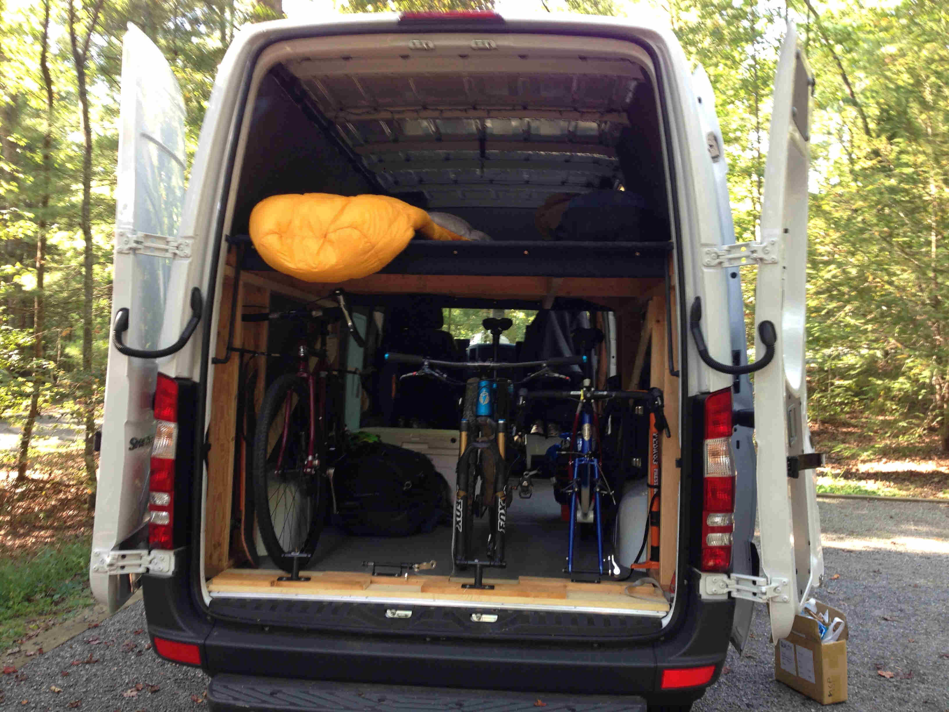 Rear view of the back of a sprinter van, with it's doors open, and bikes sitting inside
