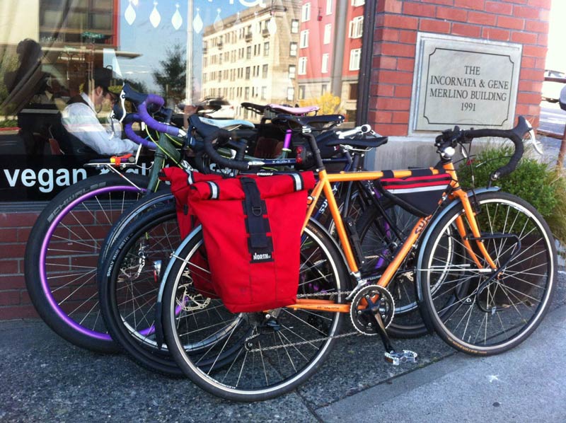 Two Surly road bikes, stacked side by side, on a sidewalk, outside of a restaurant