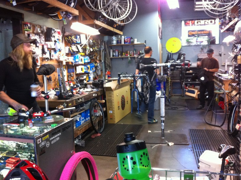 3 people standing around in a bike repair shop