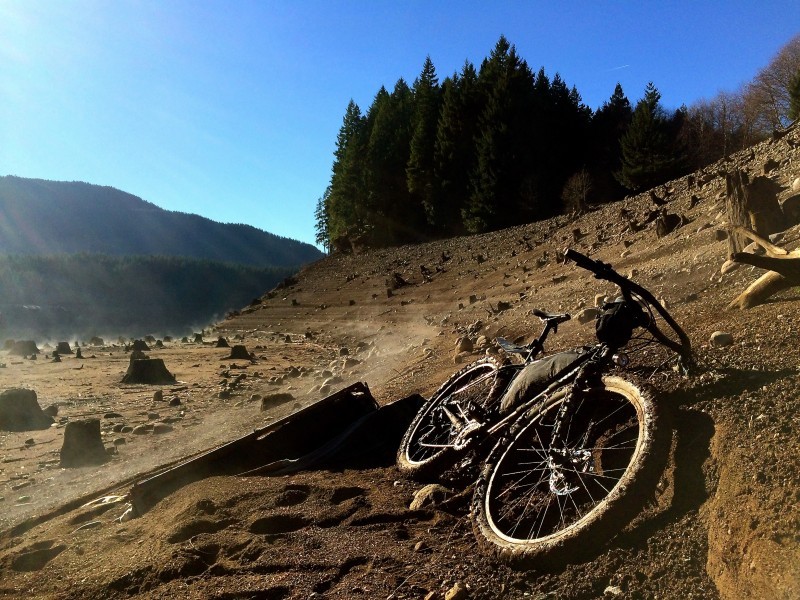 Front view of a Surly fat bike, laying on it's left side, along a dirt hill with tree stumps, with mountains behind
