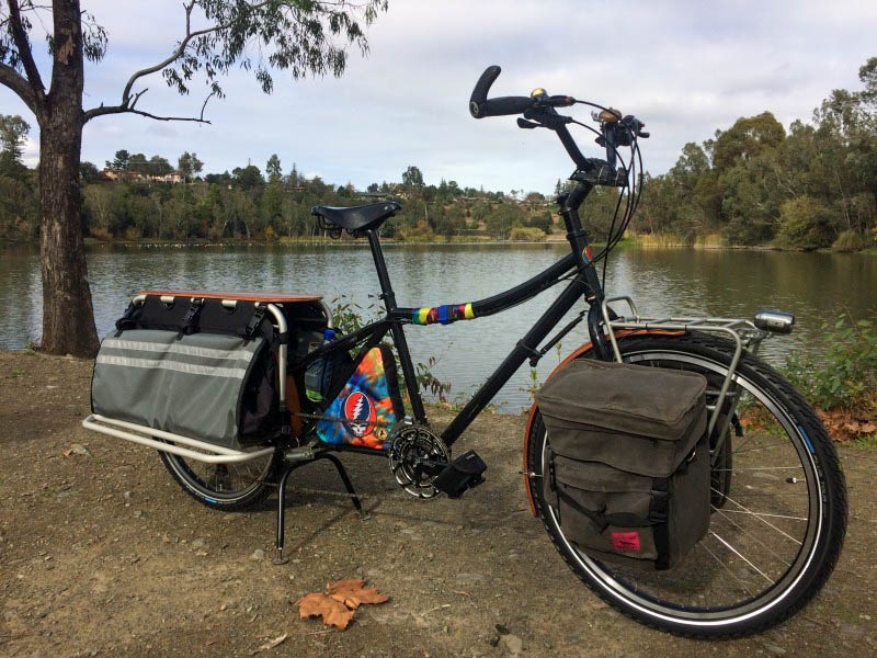 Right side view of a black Surly bike with saddle bags, on the bank of a pond, shown in the background