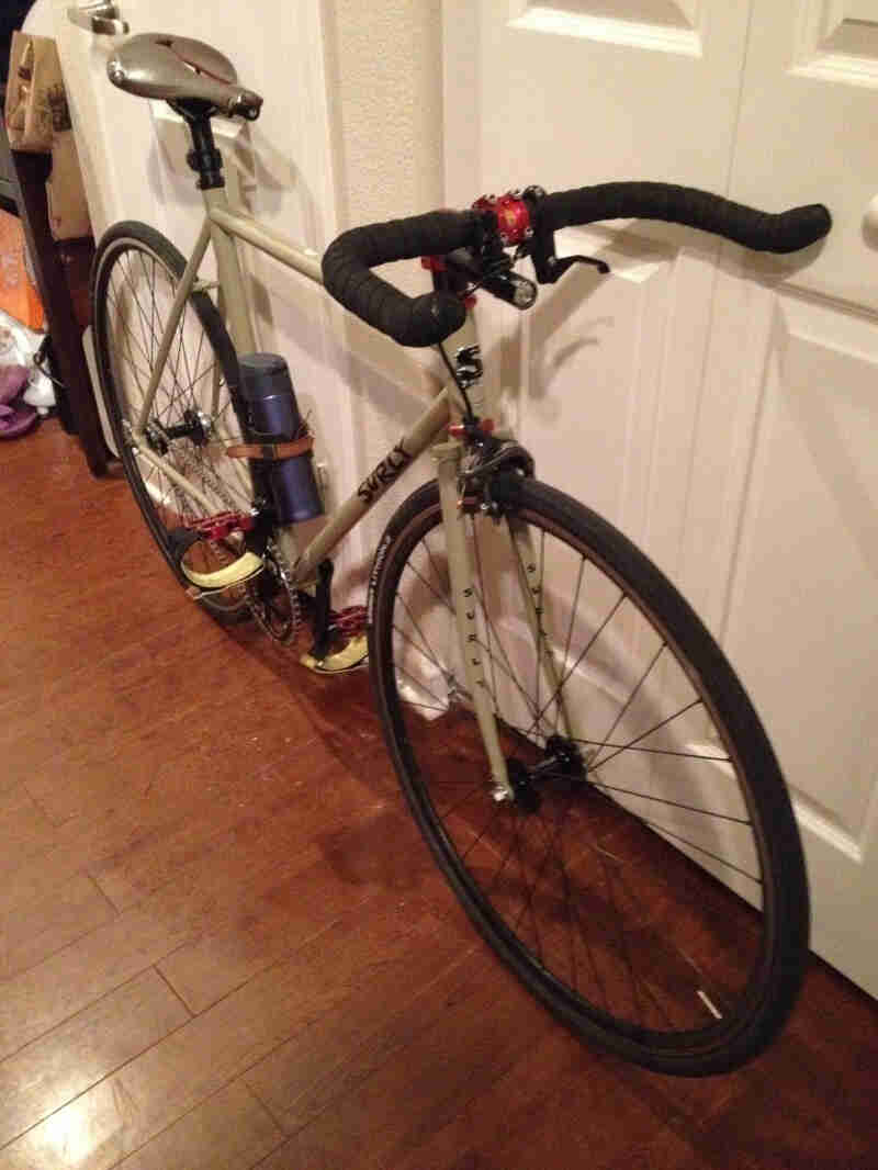 Front, right side view of a tan Surly bike, leaning against a white closet door, in a room with a wood floor