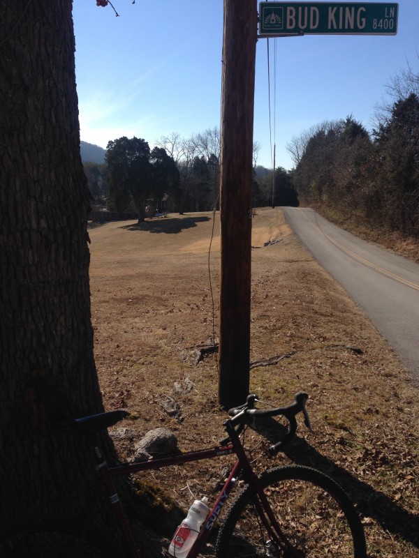 Right side view of a red Surly bike, leaning on a tree, in front of a telephone pole with a Bud King Lane street sign