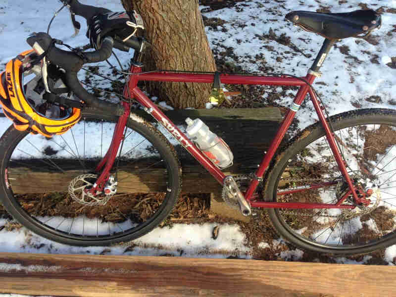 Left side view of a red Surly bike, parked between 4 x 4 timbers, on snowy ground next to a tree