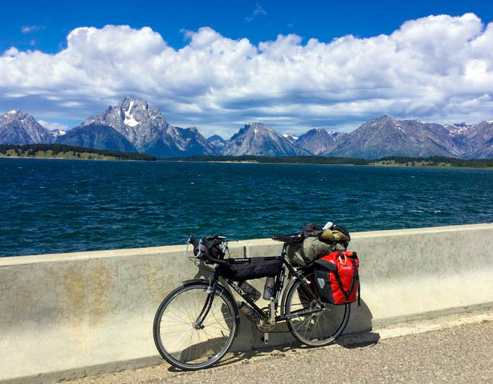 Left side view of a Surly bike with gear, leaning on a cement barrier, with a lake and mountains in the background 