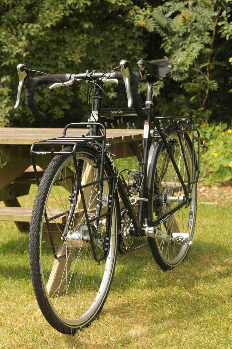 Front, left side view of a black Surly Long Haul Trucker bike, leaning on the end of a picnic table, in a grass clearing