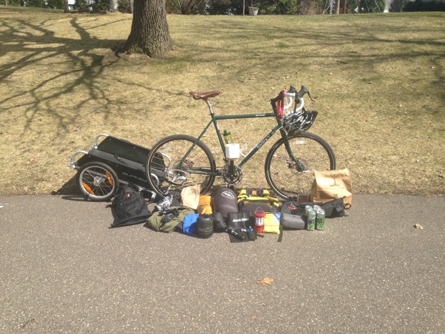Right side view of a black Surly bike with a trailer, on a paved trail, with gear laying in front of the wheels