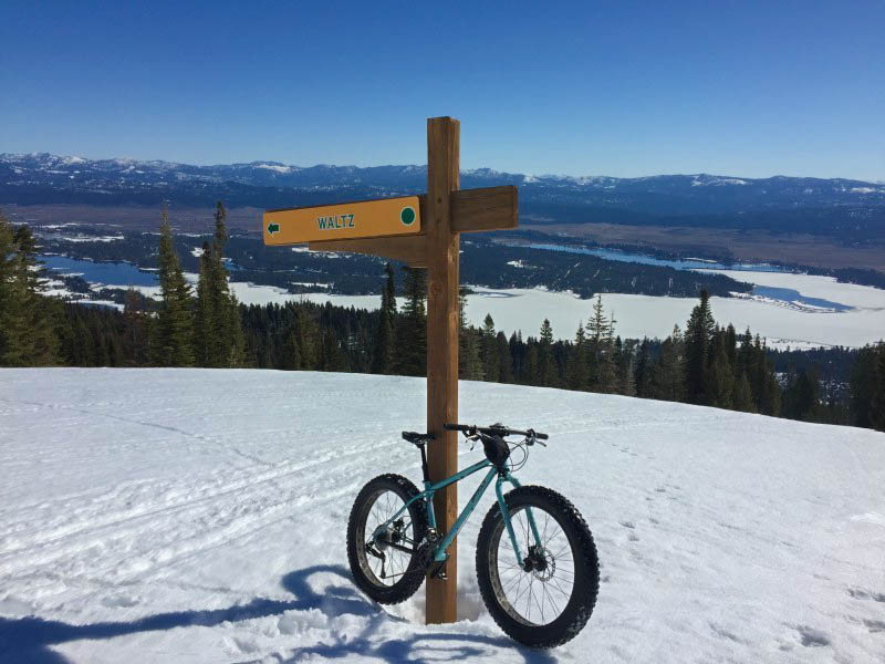 Right angled view of a Surly Wednesday MY17 fat bike, mint, parked on a snow covered hill, in front a wood post