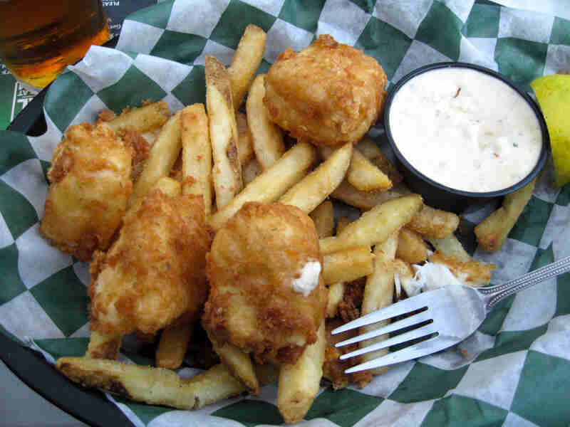 Downward view of a food basket, with fries, battered fish and a cup of tartar sauce on it