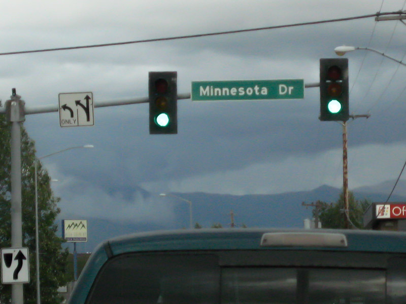 A traffic light pole, with a Minnesota Dr. sign on it, with mountains in the background on a cloudy day