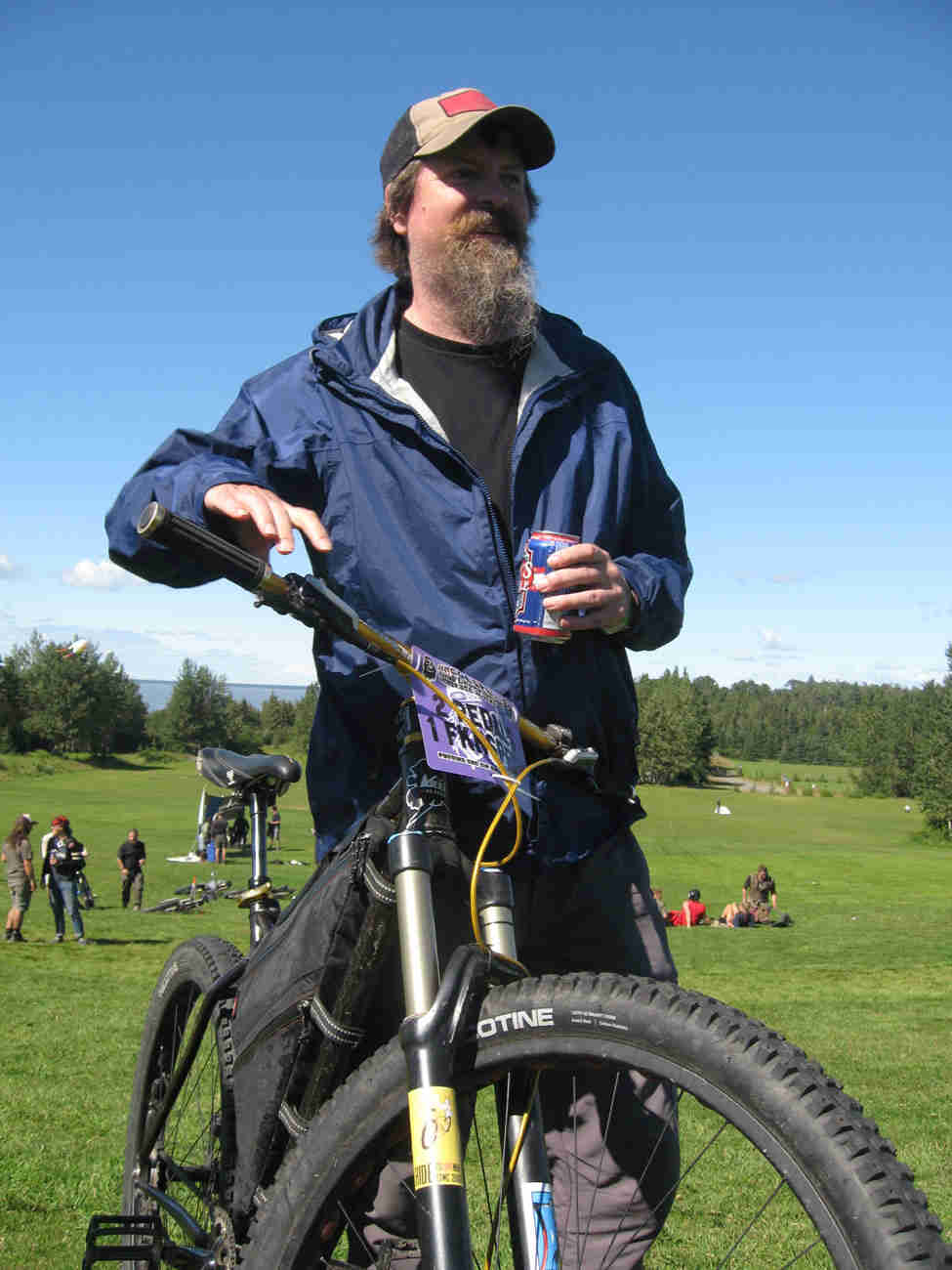 Front view of a Surly bike with a cyclist standing on the left side, on a grass field with people behind them