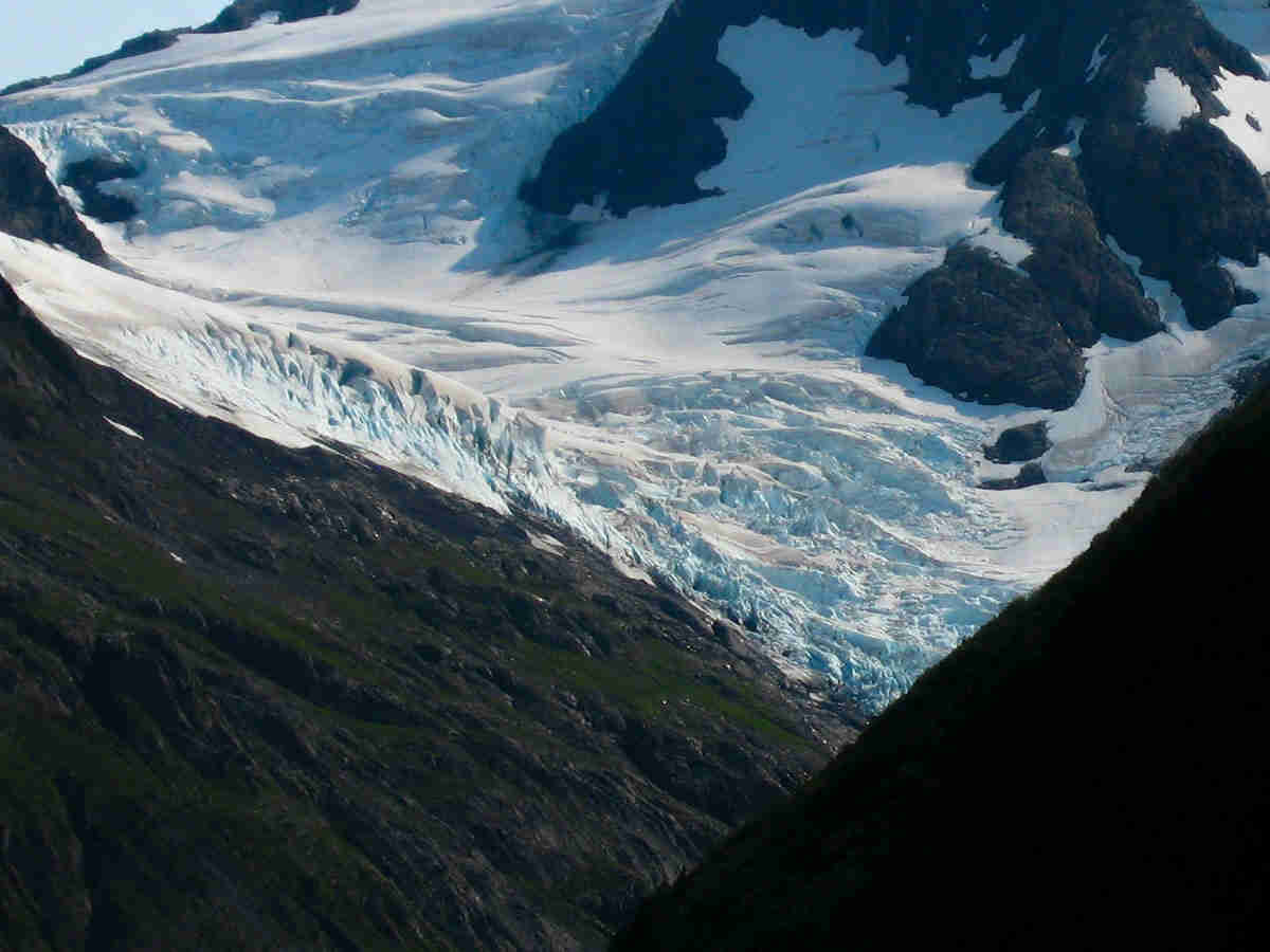 A glacier laying across the side of a mountain and the green valley below