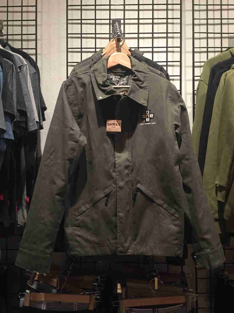 Front view of a row of Surly Waxed Jackets 2.0, hanging on a retail clothing rack, mounted to a wall