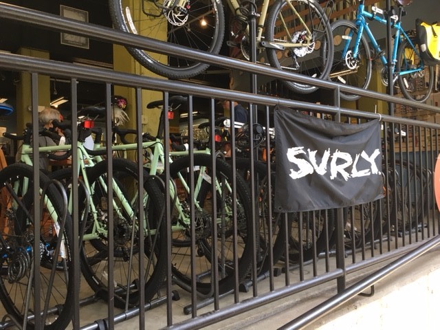 A black Surly banner hanging from a handrail with lined up bikes in the background