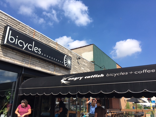 A building with a long, Angry Catfish - bicycles + coffee canopy,  leading the the front door