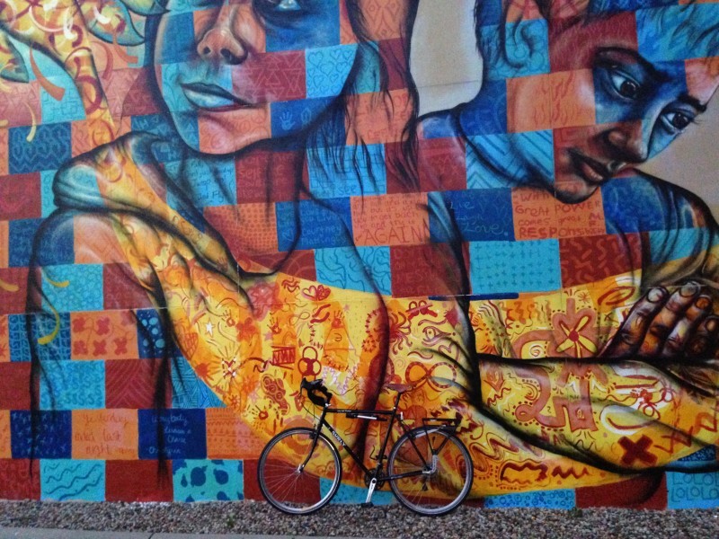 Left side view of a black Surly bike, leaning against a wall with a painted mural on it