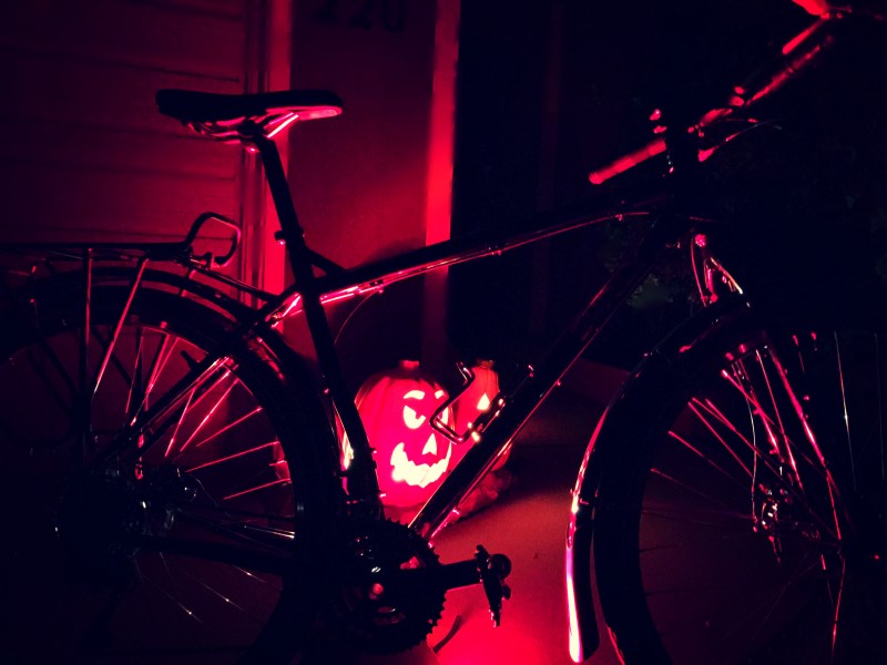 Right side view of a Surly bike parked in front of 2 plastic pumpkins with red lights inside, at nighttime