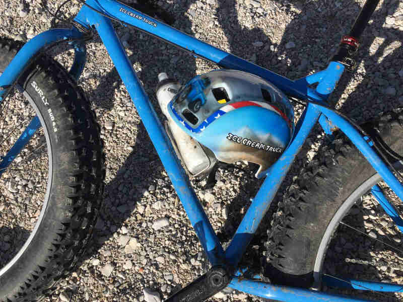 Downward view of the right side of a Surly Ice Cream Truck fat bike, blue, laying on it's side on gravel
