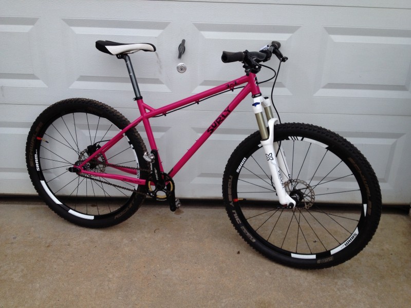 Right side view of a pink Surly 1x1 bike, leaning on the outside of a white garage door