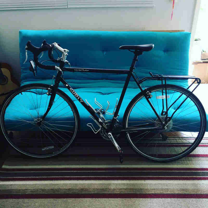 Left profile of a Surly Long Haul Trucker bike on a rug, in a room with a couch in the background