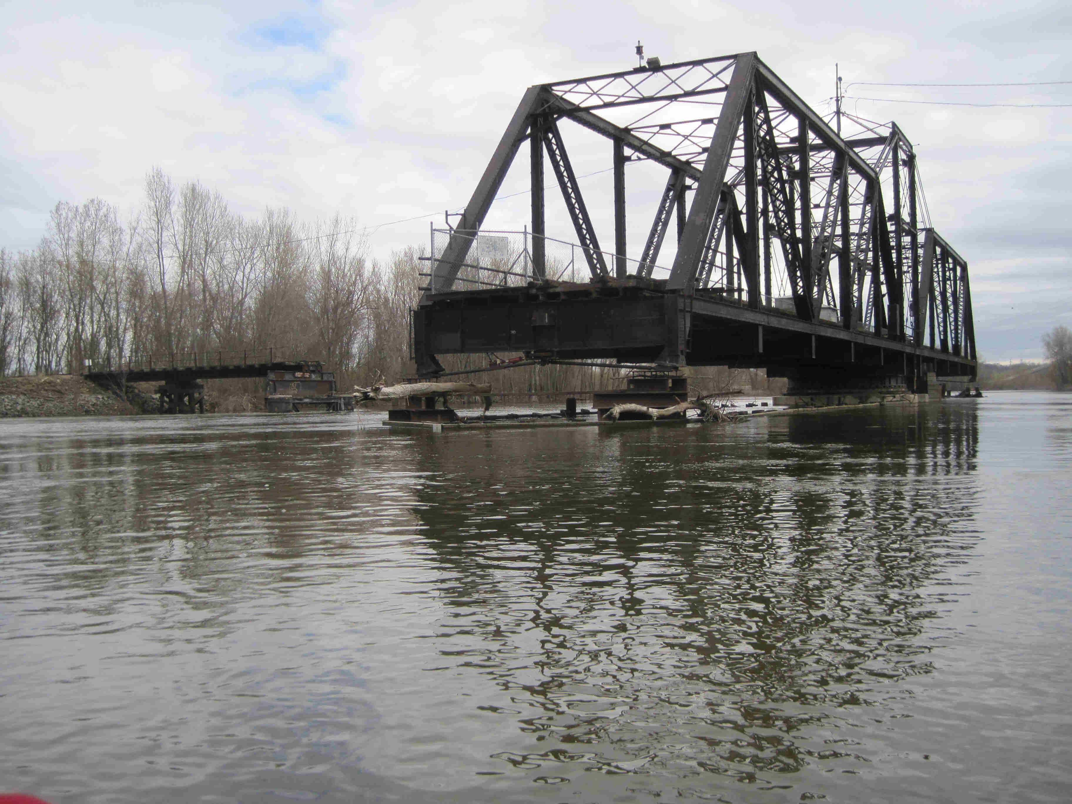 A steel swing bridge on a river, with bare trees in the background